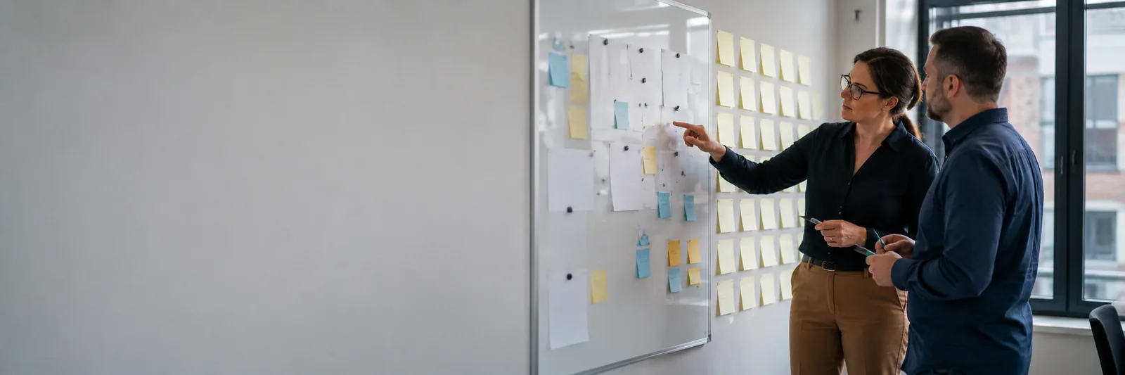 Two colleagues planning a programme at a sticky-note whiteboard